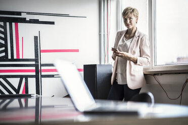 Selbstbewusste Geschäftsfrau mit Mobiltelefon in einem modernen Büro - RIBF00602