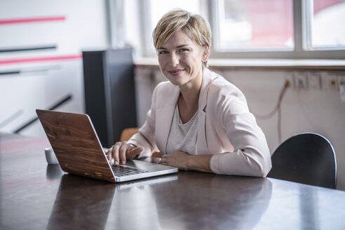 Portrait of smiling businesswoman with laptop in modern conference room - RIBF00606