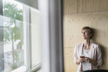 Lächelnde Geschäftsfrau, die im Büro ein Mobiltelefon benutzt - RIBF00608