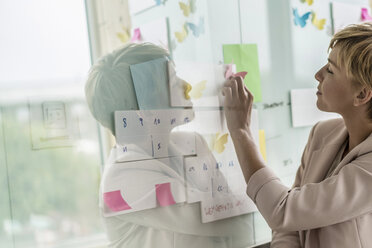 Businesswoman putting notes on whiteboard in office - RIBF00613