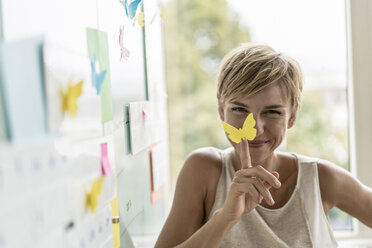 Smiling businesswoman with adhesive notes at whiteboard in modern office - RIBF00618