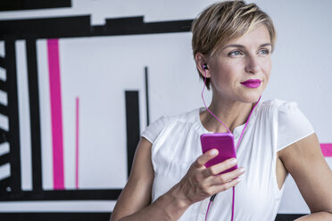 Woman in modern office listening to music on smartphone - RIBF00640