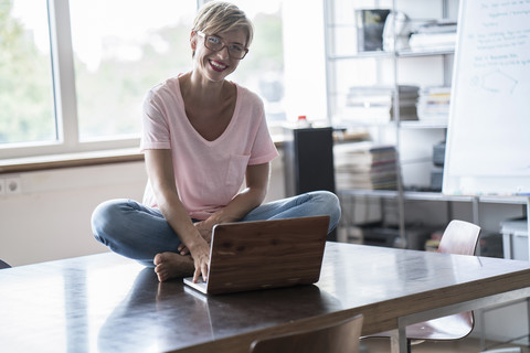 Smiling woman sitting on table using laptop stock photo