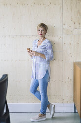 Smiling businesswoman standing at wooden wall in offce - RIBF00665