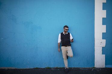 Mann lehnt an blauer Wand und schaut auf sein Handy - ZEF11628