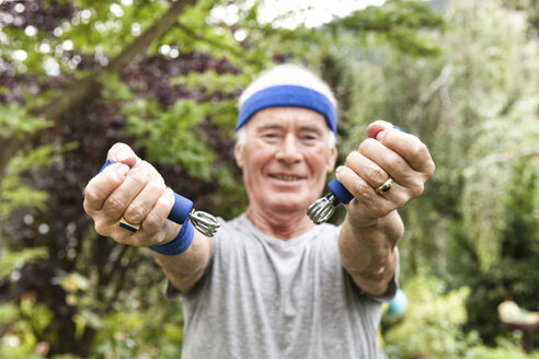 Älterer Mann beim Fitnesstraining mit Greifzange in seinem Garten - MFRF00734