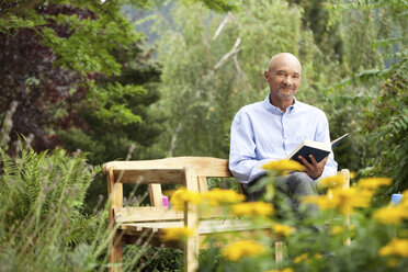 Älterer Mann sitzt auf einer Gartenbank und liest ein Buch - MFRF00752