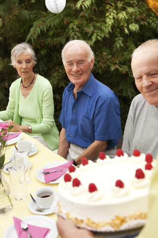 Ältere Frau serviert Sahnetorte im Garten, lizenzfreies Stockfoto