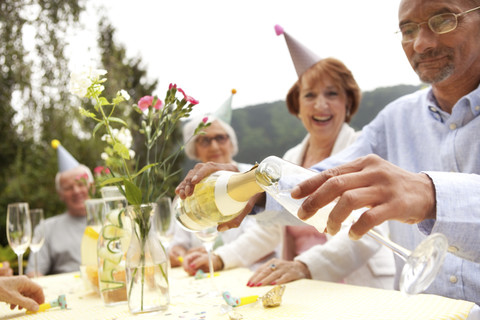 Ältere Menschen beim Feiern, Mann gießt Champagner in ein Glas, lizenzfreies Stockfoto