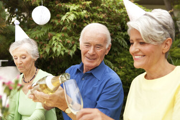 People celebrating in garden, senior man pouring champagne in glass - MFRF00780