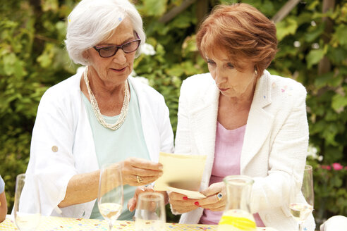 Zwei ältere Frauen schauen sich auf einer Party Fotos an - MFRF00817