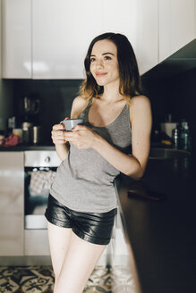 Lächelnde junge Frau trinkt Kaffee in der Küche - GIOF01632