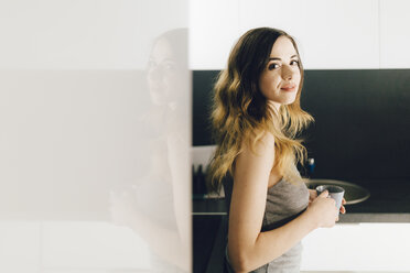 Smiling young woman drinking coffee in kitchen - GIOF01633