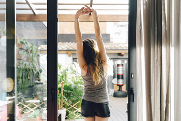 Young woman stretching at terrace door - GIOF01634