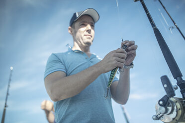 Teenage boy tying hook on fishing rod while standing at lakeshore against  cloudy sky stock photo