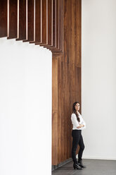 Confident businesswoman standing at wooden wall - PESF00373