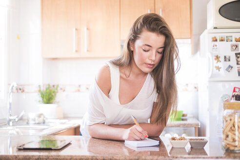 Junge Frau schreibt in der Küche auf einem Notizblock - SIPF01100