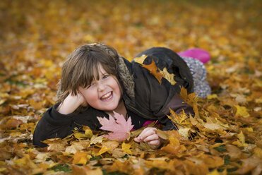 Laughing girl lying on soil covered with autumn leaves - MJOF01317