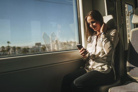 Lächelnde Frau in einem Zug, die auf ihr Mobiltelefon schaut, lizenzfreies Stockfoto