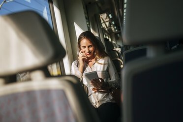 Smiling woman on a train using a tablet - KIJF00869