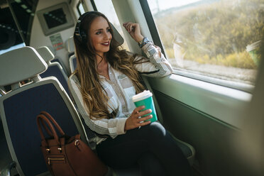 Frau in einem Zug, die mit Kopfhörern Musik hört und Kaffee trinkt - KIJF00873