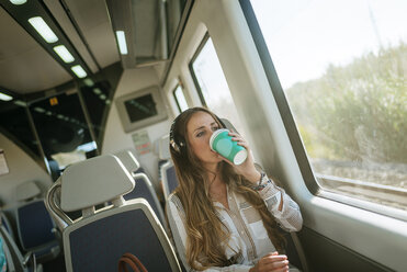 Frau in einem Zug, die mit Kopfhörern Musik hört und Kaffee trinkt - KIJF00874