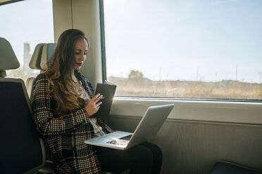 Businesswoman on a train with notebook and laptop - KIJF00880