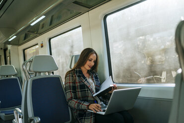 Businesswoman on a train with notebook and laptop - KIJF00881