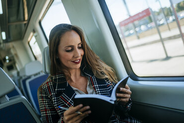 Geschäftsfrau in einem Zug mit Notizbuch - KIJF00887
