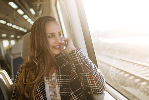 Lächelnde Frau in einem Zug, die aus dem Fenster schaut - KIJF00888