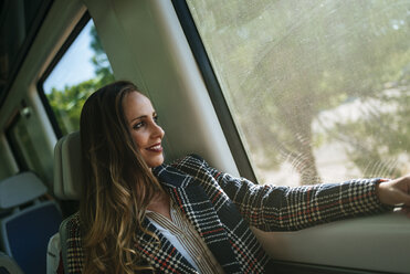 Lächelnde Frau in einem Zug, die aus dem Fenster schaut - KIJF00891