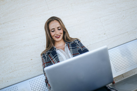 Geschäftsfrau, die auf einer Bank sitzt und einen Laptop benutzt, lizenzfreies Stockfoto