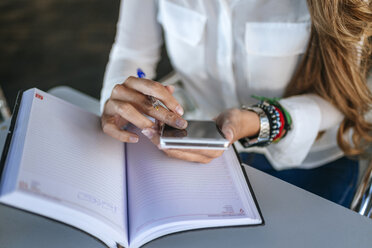 Nahaufnahme der Hände einer Frau, die ein Smartphone und ein Notebook benutzt - KIJF00906