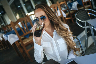 Woman drinking a cola at a street cafe - KIJF00908