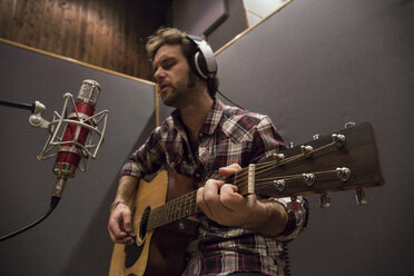 Mann spielt Gitarre in einem Aufnahmestudio während einer Musikaufnahme - ABZF01542