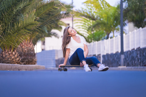 Spanien, junge Frau auf Longboard sitzend auf der Straße, lizenzfreies Stockfoto