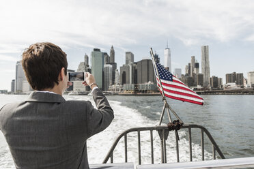 USA, Brooklyn, back view of businesswoman on a boat taking picture of Manhattan skyline - UUF09248