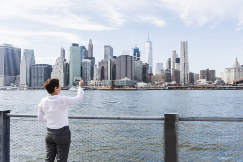USA, Brooklyn, Geschäftsfrau, die die Skyline von Manhattan fotografiert, lizenzfreies Stockfoto