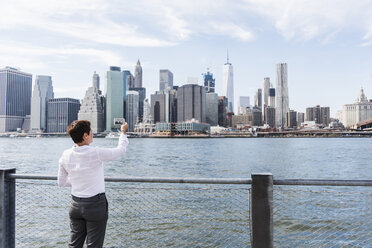 USA, Brooklyn, Geschäftsfrau, die die Skyline von Manhattan fotografiert - UUF09251