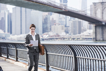 USA, Brooklyn, Geschäftsfrau beim Zeitungslesen vor den Wolkenkratzern von Manhattan - UUF09259