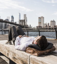 USA, Brooklyn, businesswoman lying on bench listening music with earphones - UUF09264