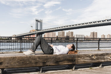 USA, Brooklyn, businesswoman lying on bench listening music with earphones - UUF09265