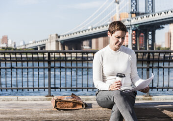 USA, Brooklyn, Geschäftsfrau sitzt auf einer Bank und liest Dokumente - UUF09268