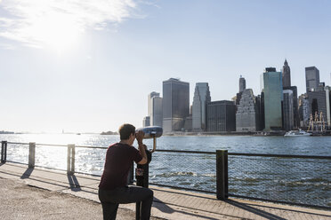 USA, Brooklyn, woman looking at Manhattan skyline with coin operated binoculars - UUF09271