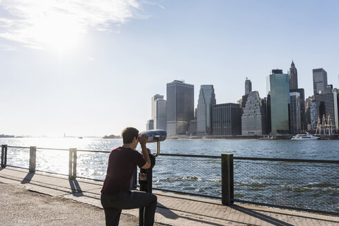 USA, Brooklyn, Frau betrachtet die Skyline von Manhattan mit einem münzbetriebenen Fernglas - UUF09271