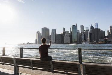 USA, Brooklyn, Rückenansicht einer Frau, die mit ihrem Handy die Skyline von Manhattan fotografiert - UUF09273