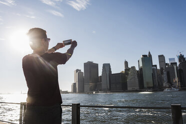 USA, Brooklyn, back view of woman taking picture of Manhattan skyline with cell phone - UUF09274