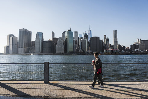 USA, Brooklyn, Geschäftsfrau schaut auf ihr Smartphone vor der Skyline von Manhattan - UUF09278