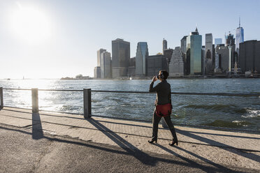 USA, Brooklyn, businesswoman drinking coffee to go in front of Manhattan skyline - UUF09279