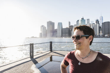 USA, Brooklyn, Porträt einer lächelnden Frau mit Sonnenbrille vor der Skyline von Manhattan - UUF09281